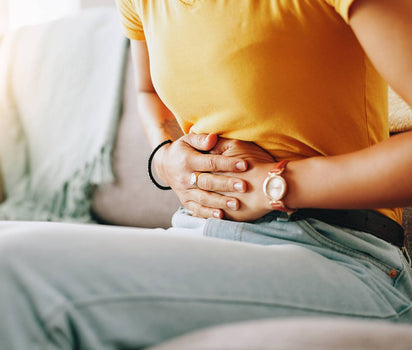 Woman in yellow t-shirt holding her stomach on sofa — probiotic live cultures support bloating, digestion and gut balance