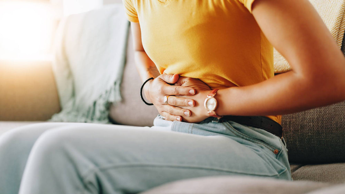 Woman in yellow t-shirt holding her stomach on sofa — probiotic live cultures support bloating, digestion and gut balance