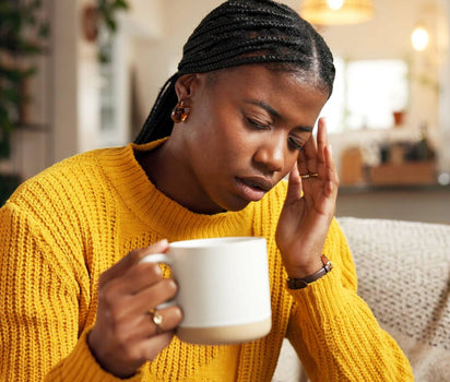 Tired woman in yellow jumper holding mug with hand on temple — omega-3 supports brain fog, joint and mood health