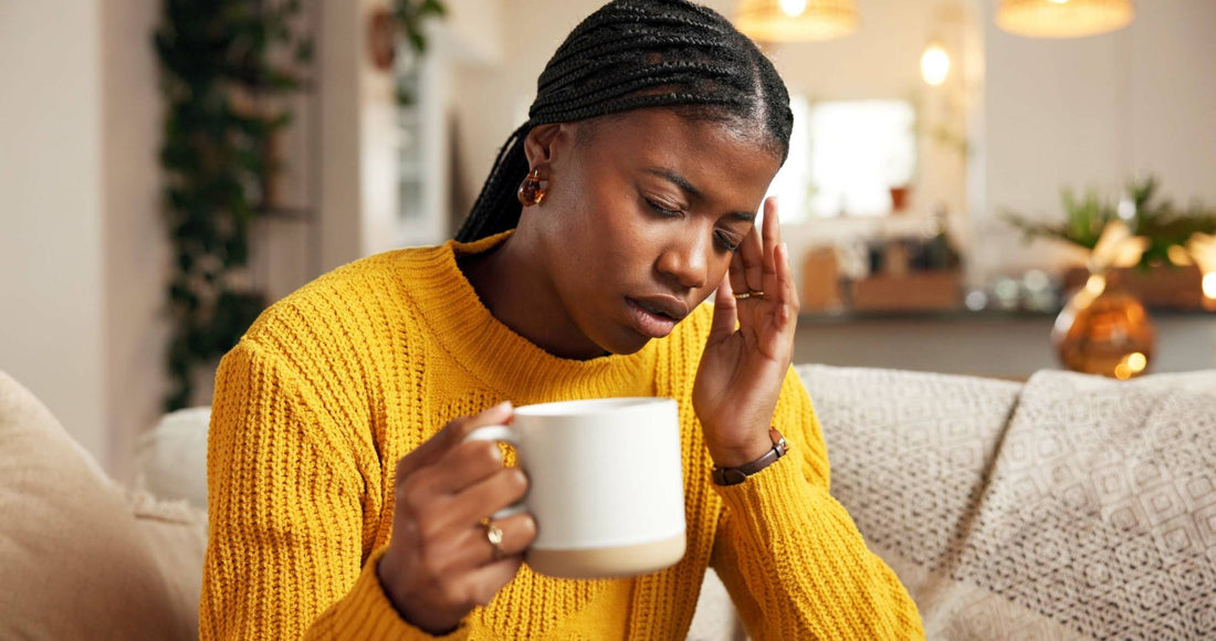 Tired woman in yellow jumper holding mug with hand on temple — omega-3 supports brain fog, joint and mood health
