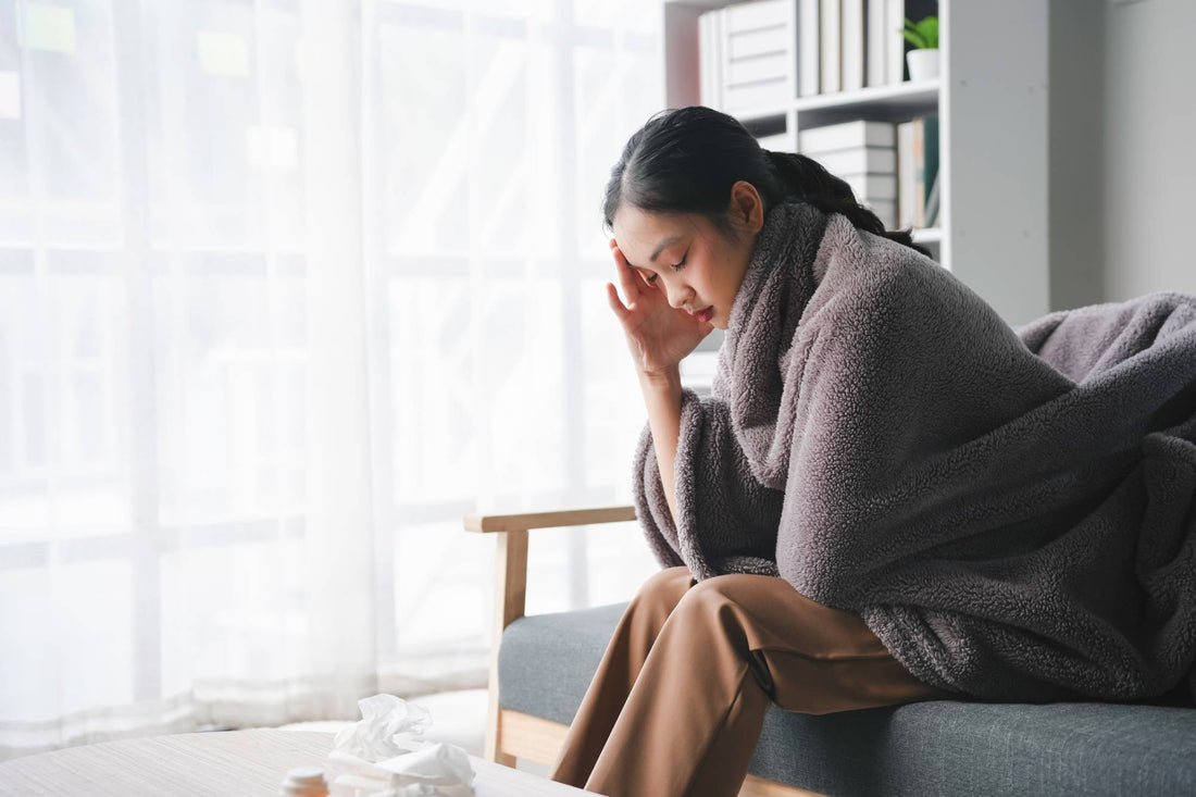 Woman wrapped in blanket on sofa with head in hand — daily multivitamin supports energy and micronutrient gaps