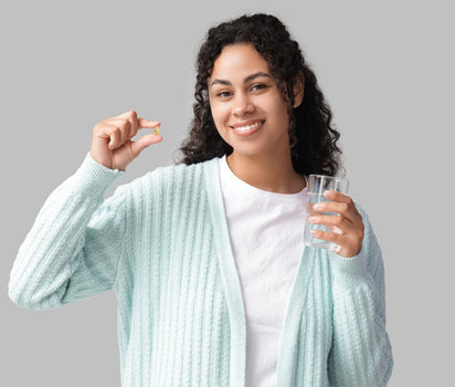 Smiling woman holding omega-3 capsule and glass of water — EPA and DHA support heart, brain and overall health