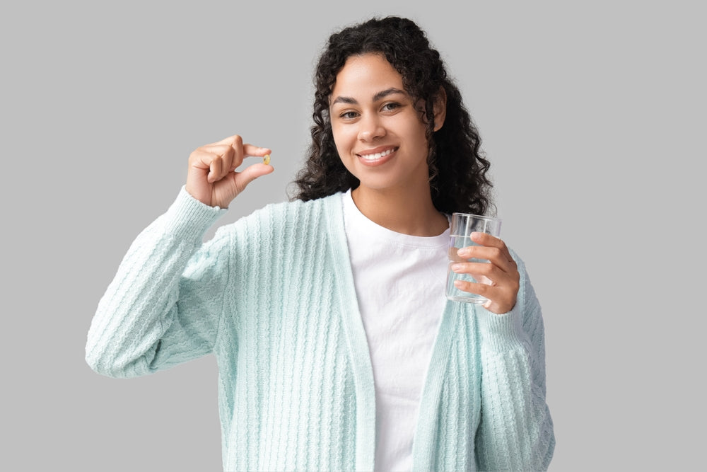 Smiling woman holding omega-3 capsule and glass of water — EPA and DHA support heart, brain and overall health