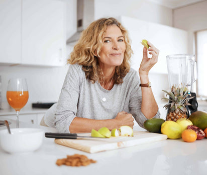 Daily multivitamin supports absorption and everyday wellbeing — mature woman eating fresh fruit in kitchen