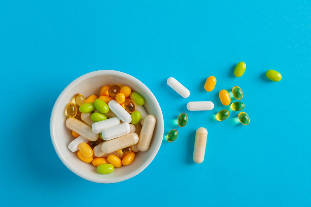 Bowl of mixed vitamin capsules and tablets on blue background — daily multivitamin supports energy and overall health