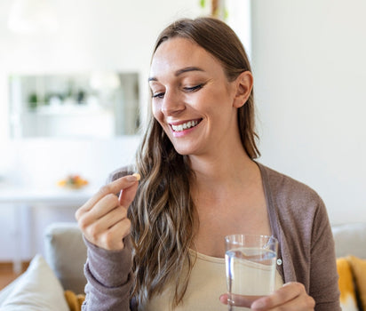 Smiling woman taking a capsule with glass of water at home — probiotic live cultures support gut health and bloating