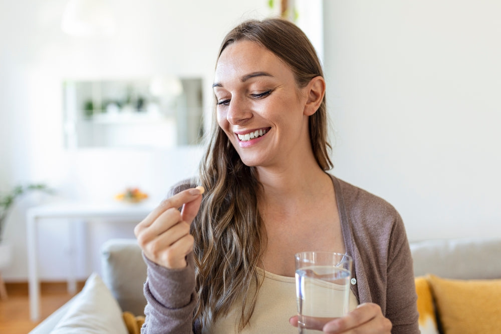 Smiling woman taking a capsule with glass of water at home — probiotic live cultures support gut health and bloating