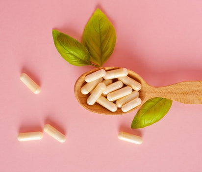 Supplement capsules on wooden spoon with basil leaves on pink background — collagen and magnesium support evening routine