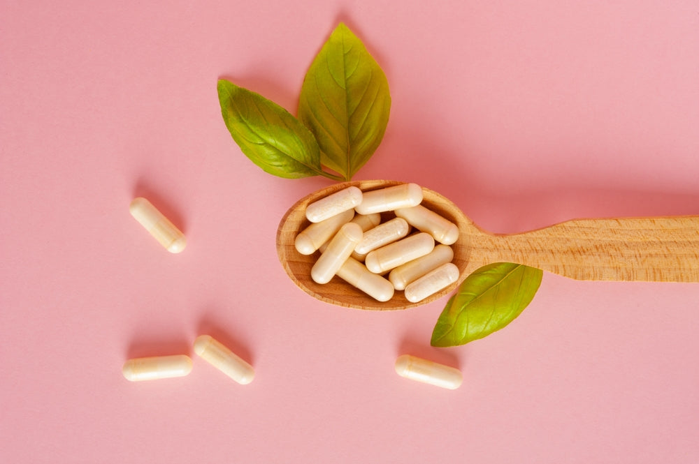 Supplement capsules on wooden spoon with basil leaves on pink background — collagen and magnesium support evening routine