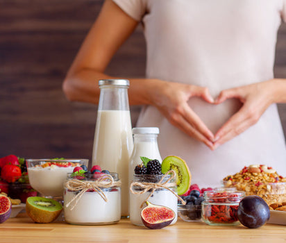 Woman framing stomach with hands beside healthy foods, yogurts and berries — magnesium and multivitamin support energy and metabolism