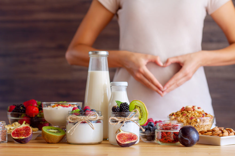 Woman framing stomach with hands beside healthy foods, yogurts and berries — magnesium and multivitamin support energy and metabolism