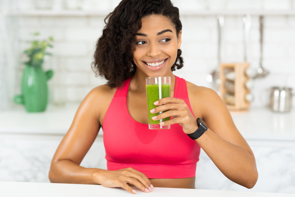 Smiling woman in pink sports top drinking green smoothie in kitchen — daily multivitamin and omega-3 support immune resilience