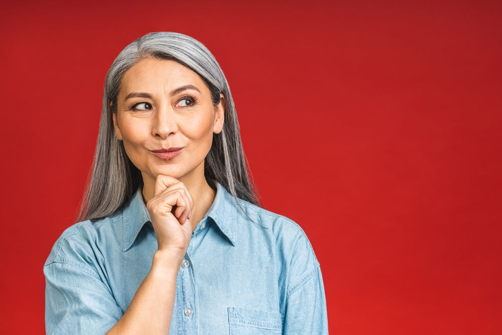 Magnesium supports menopause symptoms, sleep and mood — mature woman with grey hair on red background