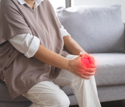 Person holding painful knee on sofa — glucosamine and collagen support cartilage and mobility