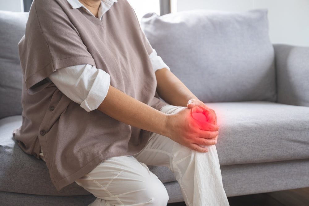 Person holding painful knee on sofa — glucosamine and collagen support cartilage and mobility