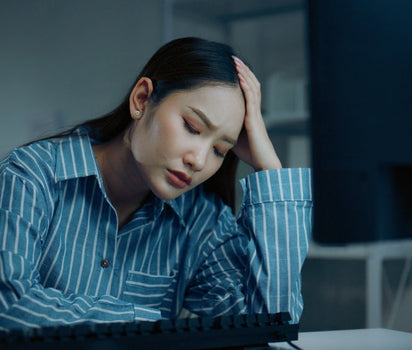 Magnesium and multivitamin support mood balance and stress — woman in striped shirt with head in hand at desk
