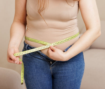Woman measuring waist with tape measure in jeans — multivitamin and magnesium support metabolism and energy production