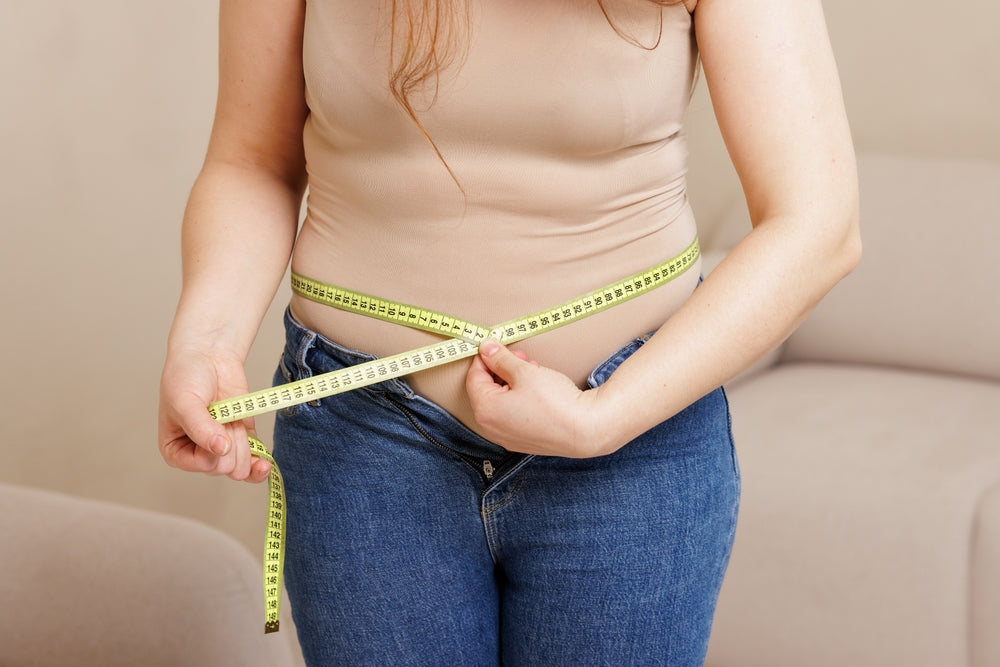 Woman measuring waist with tape measure in jeans — multivitamin and magnesium support metabolism and energy production